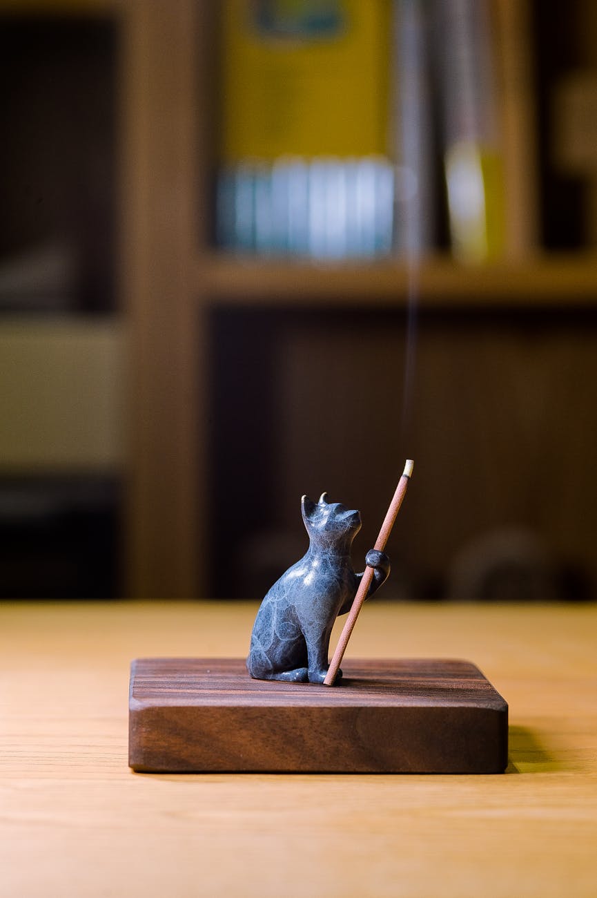 Cat figurine incense holder releasing smoke, set on a wooden base in a calm, indoor environment.